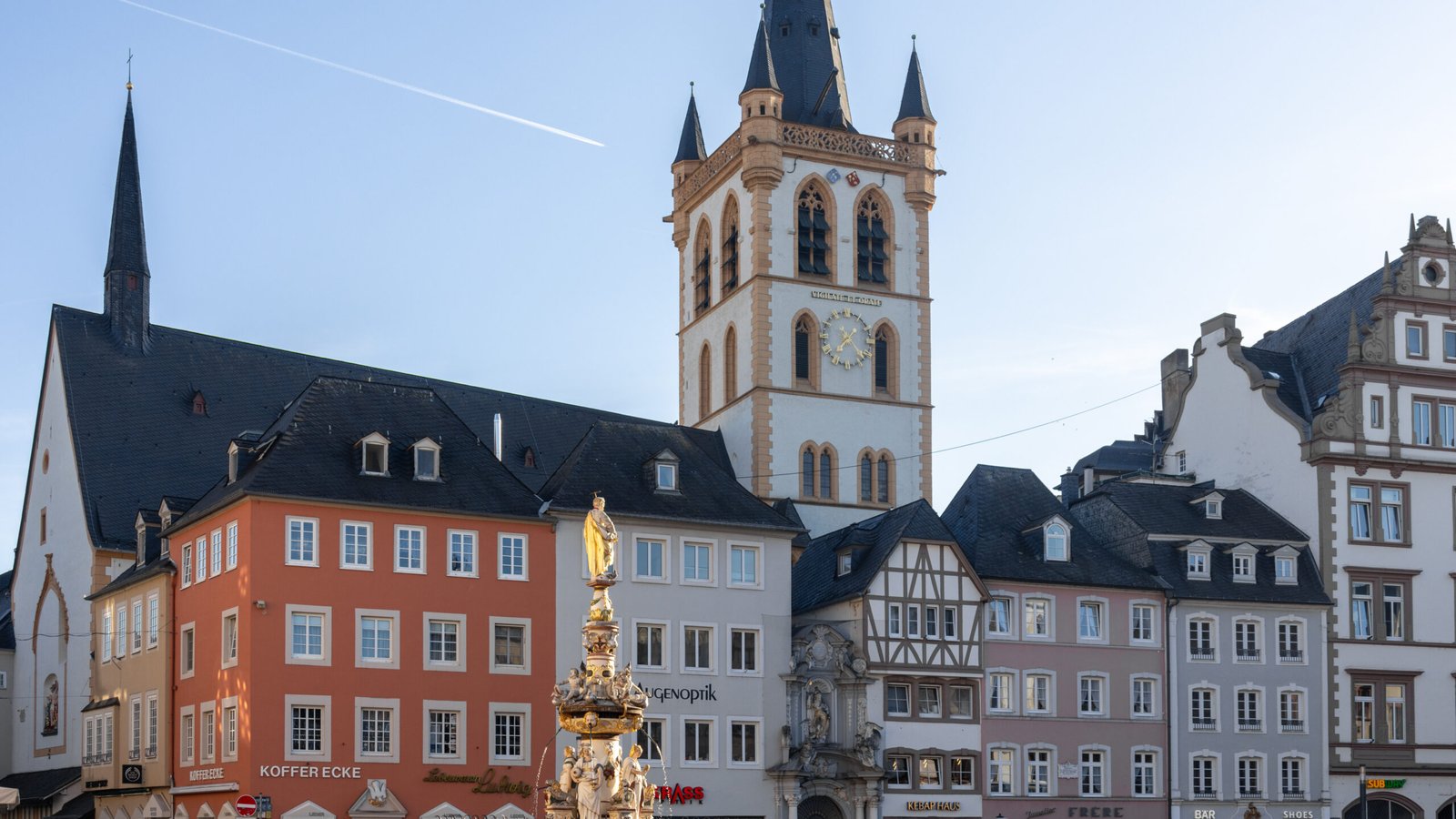 Trier Squrae | Krista the Explorer | Krista the Explorer Historic town square with a tall church tower and clock, flanked by colorful pastel buildings under a clear blue sky.
