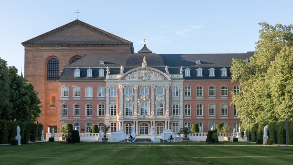 Electoral Palace Trier | Krista the Explorer Front view of a pink baroque palace with white ornate sculptures.