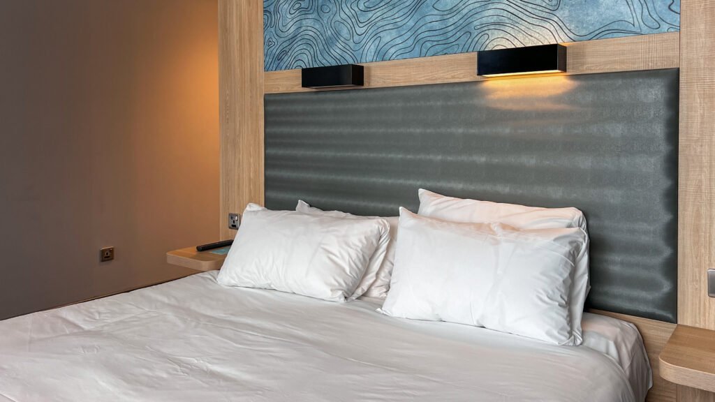 Aloft Aberdeen TECA | Krista the Explorer Hotel bed with white sheets and pillows against a gray upholstered headboard.