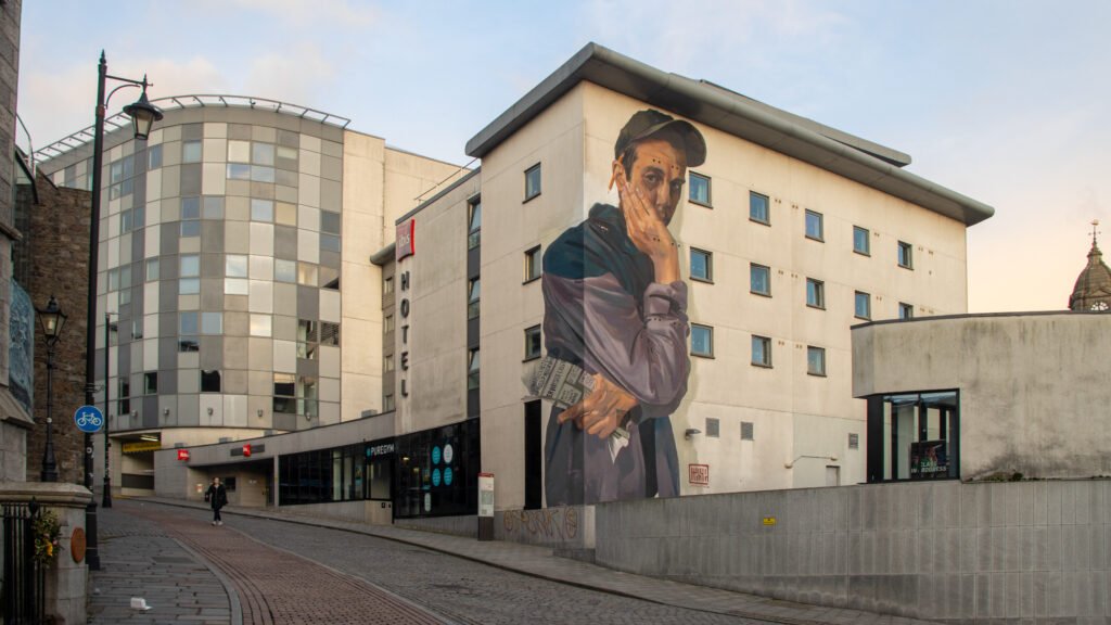 Street Art Aberdeen | Krista the Explorer Large mural of a man touching his face on the side of a beige hotel building.