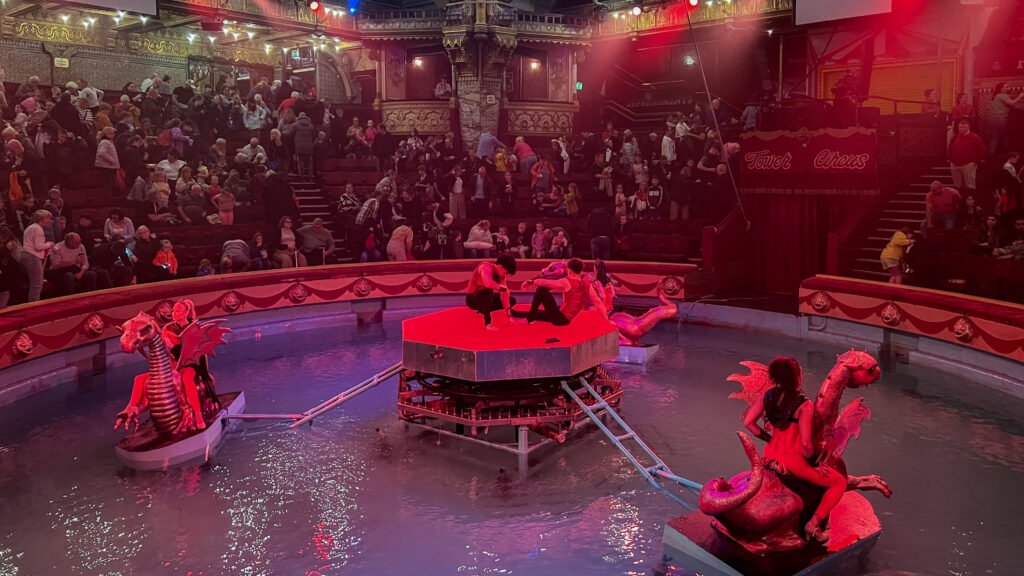 The Blackpool Tower Circus | Krista the Explorer Circus ring with performers on a red hexagonal platform in a shallow pool.