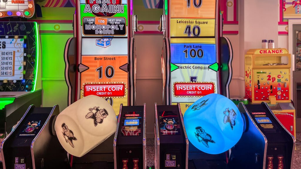 Blackpool Amusements | Krista the Explorer Row of brightly lit arcade slot machines with neon accents, displaying'Insert Coin' panels and large numbers.