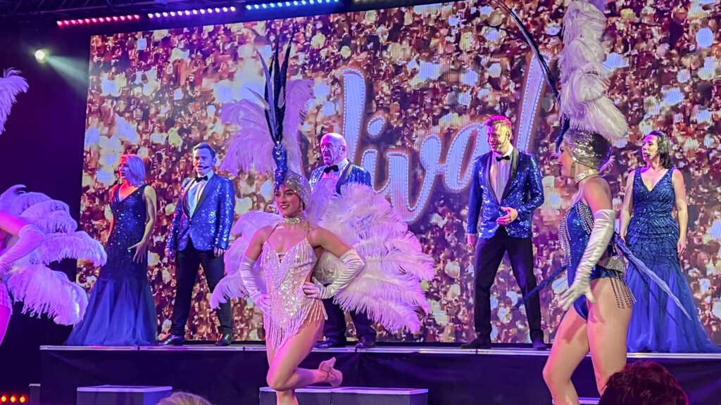 Viva Blackpool | Krista the Explorer Performers in glittery blue costumes with large feather headdresses on a stage.