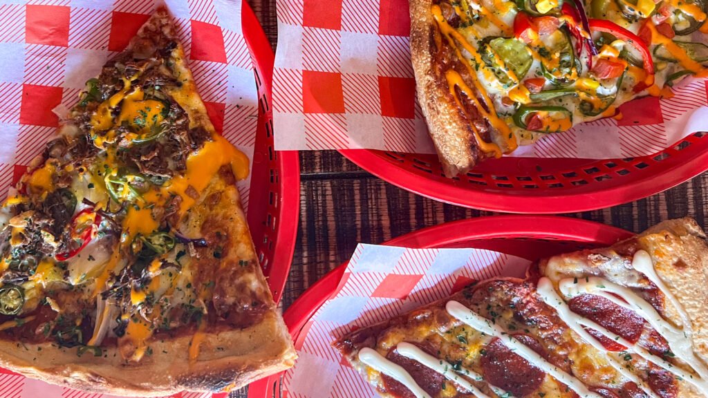 Dirty Blondes Blackpool | Krista the Explorer Assorted pizza slices with melted cheese, peppers, and herbs in red baskets on checkered paper.