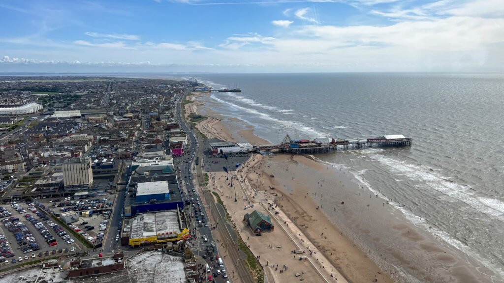 The Blackpool Tower | Krista the Explorer Aerial view of a coastal town with a long pier, sandy beach, and dense grid of buildings.