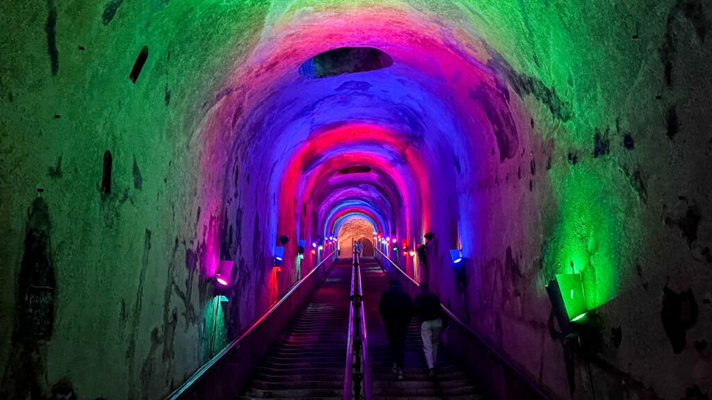 Champagne Cellar Reims | Krista the Explorer Colourful illuminated tunnel with arched ceiling, green, pink, and blue lights along a stairway.