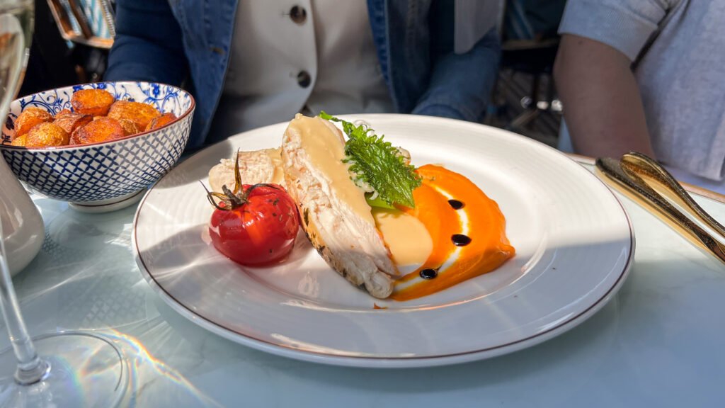 Le Réfectoire Reims | Krista the Explorer Plate with sliced chicken in orange sauce, garnished with greens and a roasted tomato.