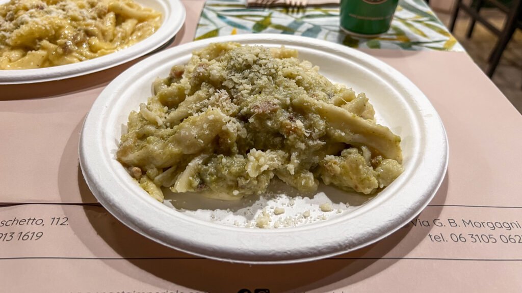 Pasta Imperiale Rome | Krista the Explorer Creamy green pasta dish with grated cheese on top served on a white disposable plate at a table.