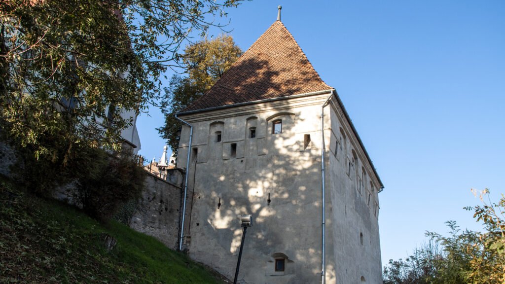 Historic stone building with a tall, steep red-tiled roof against a clear blue sky.