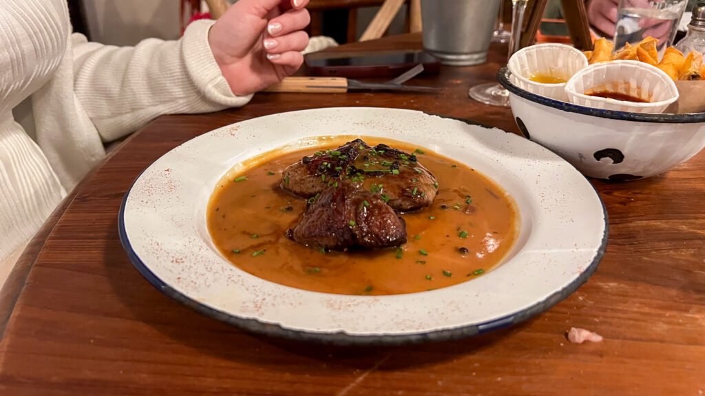 Le Tablier Reims | Krista the Explorer Plate with two beef medallions in orange sauce, garnished with chopped chives.