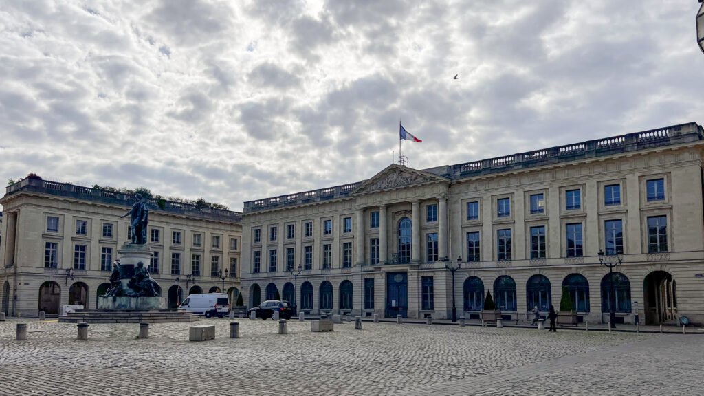 Place Royale Reims | Krista the Explorer Statue fountain in a cobblestone plaza with a grand beige stone building.