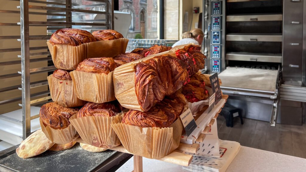 Case à Pain Reims | Krista the Explorer Stacked trays of bread on a wooden rack in a bakery shop.