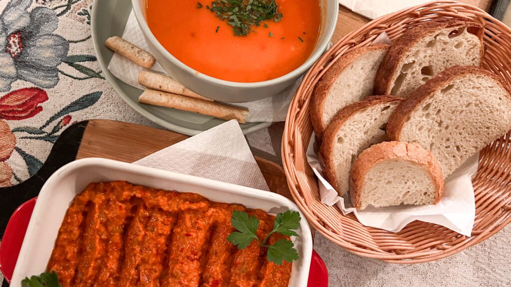 Bowl of orange soup garnished with chopped herbs and aubergine dish.