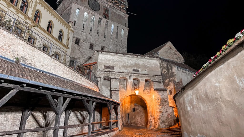 Night view of a historic stone building and tower along a narrow cobblestone alley.