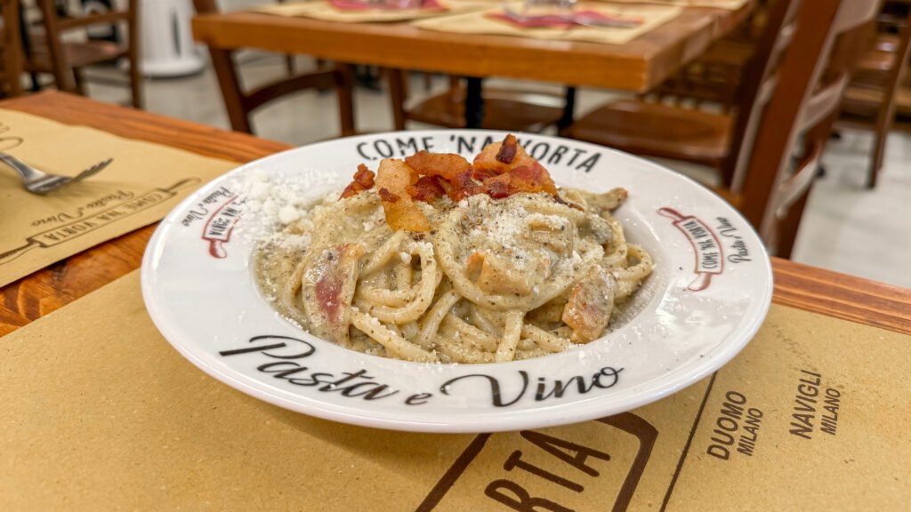 Come 'na Vorta Pasta e Vino Rome | Krista the Explorer Plate of creamy pasta with bacon bits and grated cheese in a rustic Italian restaurant setting.