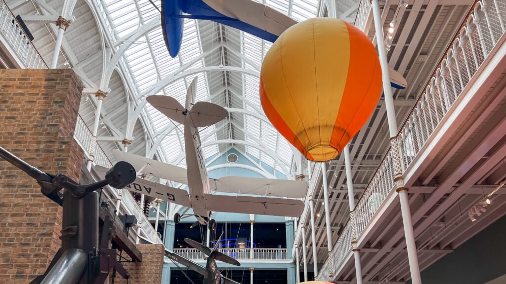 National Museum of Scotland Edinburgh | Krista the Explorer Large orange-yellow hot air balloon suspended from the ceiling in a museum.