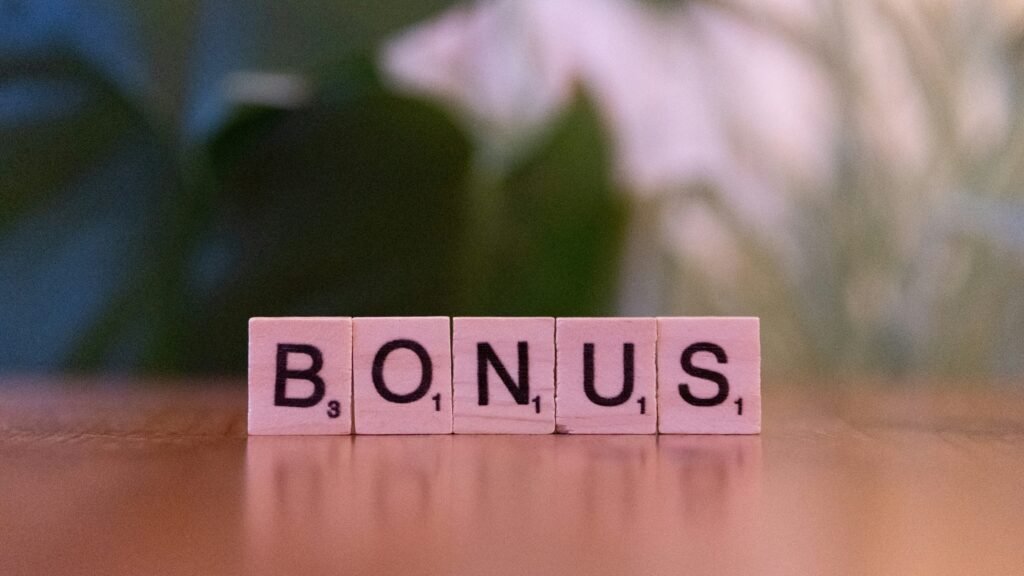 Pink Scrabble tiles spell the word BONUS on a wooden surface.