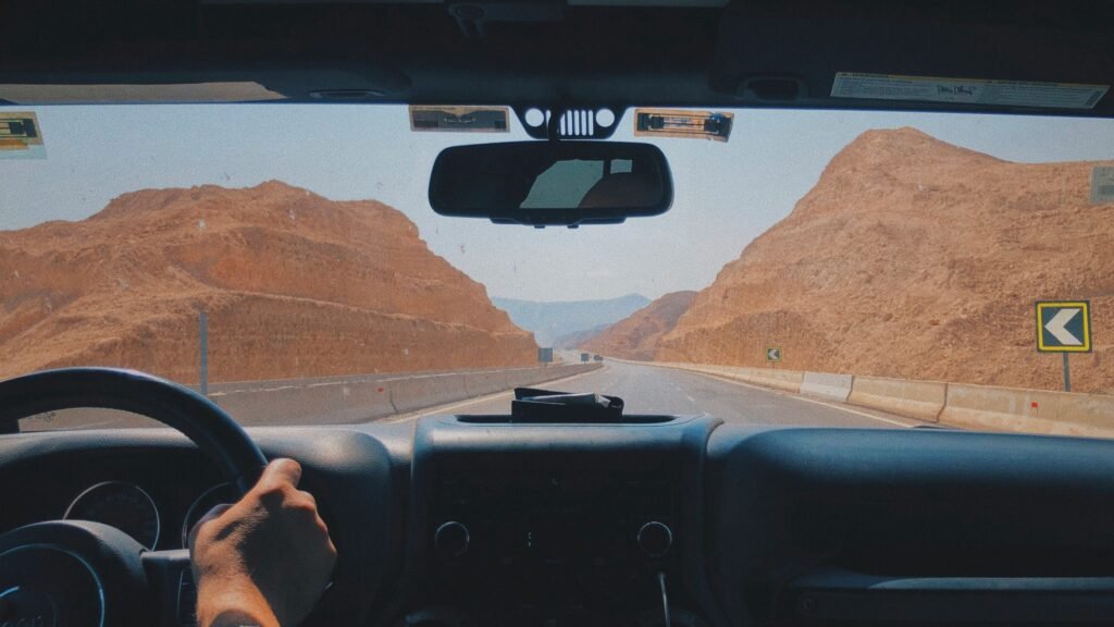EconomyBookings | Krista the Explorer Driver's hands on the steering wheel as a desert highway curves ahead.