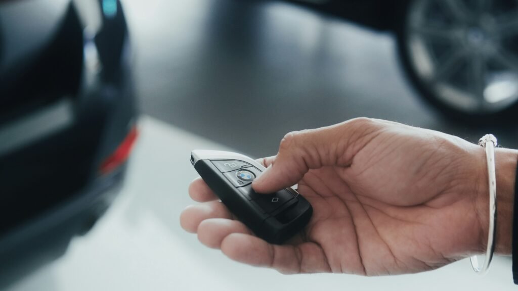 Hand holding a BMW car key fob, close to a car in the background.